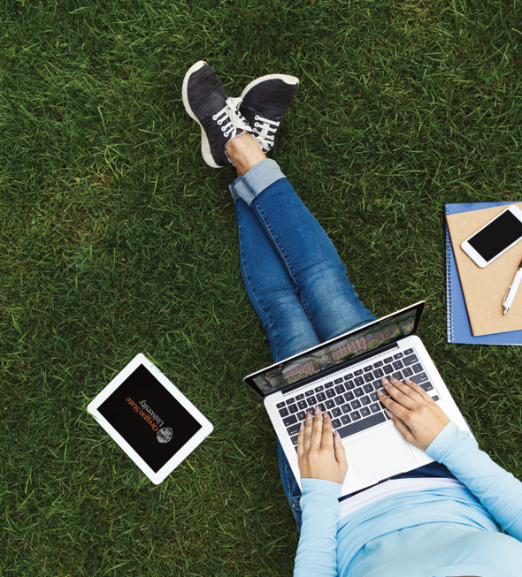 A woman sitting in the grass working on her laptop